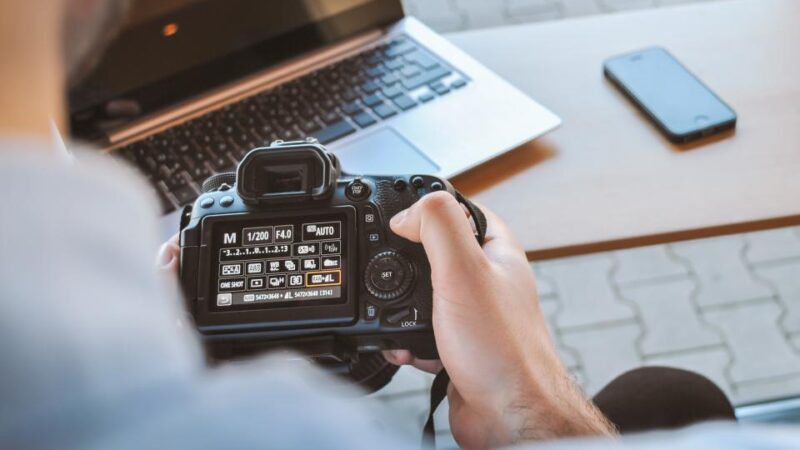 Fotograf sprawdzający zdjęcia na aparacie obok laptopa