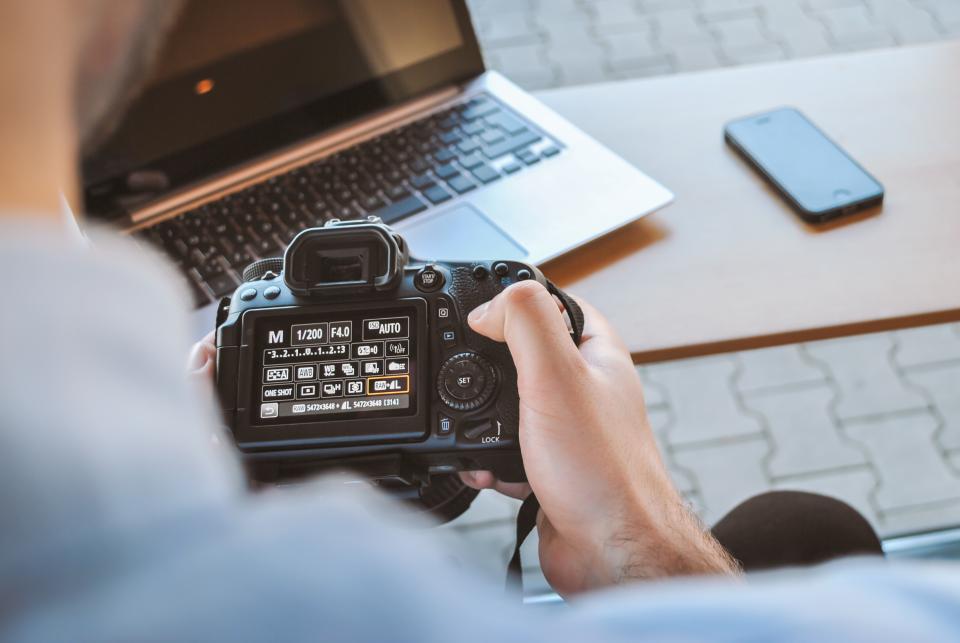 Fotograf sprawdzający zdjęcia na aparacie obok laptopa